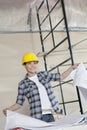 Happy mid adult worker holding building plans while looking away