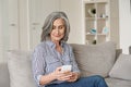 Happy mid age senior woman using smartphone sitting on sofa at home.