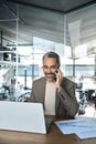 Happy mature business man ceo talking on cell phone working on laptop in office. Royalty Free Stock Photo