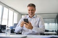 Happy mid aged business man executive using mobile phone at work in office. Royalty Free Stock Photo