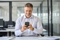 Happy mid aged business man executive using mobile phone at work in office. Royalty Free Stock Photo