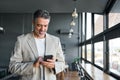 Happy mid aged business man holding cellphone using mobile phone in office. Royalty Free Stock Photo