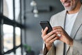 Happy mid aged business man standing in office holding mobile using cell phone. Royalty Free Stock Photo