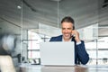 Happy mid aged business man talking on mobile phone working on laptop in office. Royalty Free Stock Photo