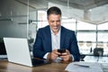Happy mid aged business man wearing suit sitting in office using mobile phone. Royalty Free Stock Photo