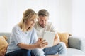 Happy mid aged couple relaxing on the sofa at home and using touchpad Royalty Free Stock Photo