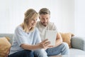 Happy mid aged couple relaxing on the sofa at home and using touchpad Royalty Free Stock Photo
