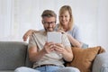 Happy mid aged couple relaxing on the sofa at home and using touchpad Royalty Free Stock Photo