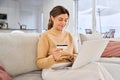 Happy mid aged woman using laptop holding credit card sitting on sofa at home. Royalty Free Stock Photo