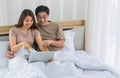 Happy middle age Asian couple dressed casually sitting relaxed on a bed at home enjoy looking at a laptop computer. Warmth,