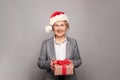 Happy middle age senior woman Santa holding Christmas present box and smiling over grey background Royalty Free Stock Photo