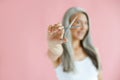 Happy middle aged Asian woman poses on pink background, focus on hand with scissors