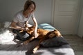 Happy middle-aged blonde lady plays with sleepy Vizsla dog on bed in sunny morning Royalty Free Stock Photo