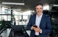 Happy middle aged business man ceo standing in office using smartphone. Royalty Free Stock Photo