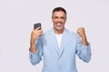 Happy middle aged business man holding phone celebrating online win, isolated. Royalty Free Stock Photo