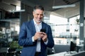 Happy middle-aged business man wearing suit using smartphone in office. Royalty Free Stock Photo