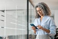 Happy middle aged business woman using mobile phone standing in office. Royalty Free Stock Photo