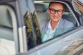 Happy middle aged business woman wearing eyeglasses looking out of a car window while sitting on back seat, she is going Royalty Free Stock Photo