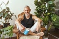 Happy middle aged caucasian man drinking morning coffee while sitting in lotus pose on the terrace of his modern flat