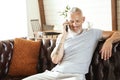 Happy middle aged caucasian man talking by mobile phone and smiling while sitting on sofa and working from home