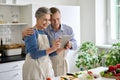 Happy middle aged couple preparing salad using tablet in kitchen. Royalty Free Stock Photo