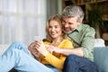 Happy Middle Aged Couple Relaxing With Smartphone On Couch At Home Royalty Free Stock Photo