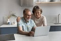 Happy middle aged couple using computer in kitchen. Royalty Free Stock Photo