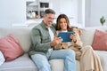 Happy middle aged couple using digital tablet relaxing on couch at home. Royalty Free Stock Photo