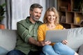 Happy Middle Aged Couple Using Laptop While Relaxing On Couch At Home Royalty Free Stock Photo