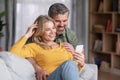 Happy middle aged couple using smartphone while relaxing on couch at home Royalty Free Stock Photo