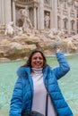 happy middle aged female tourist on vacation throwing a coin in the water of famous trevi fountain in rome Royalty Free Stock Photo