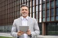Happy middle aged business man executive in suit using tablet standing outdoors. Royalty Free Stock Photo