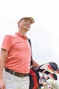 Happy middle-aged man looking away while carrying golf bag against clear sky