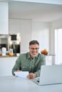 Happy middle aged man looking at paper bill working on laptop at home. Royalty Free Stock Photo