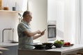 Happy middle aged man using cellphone, cooking in kitchen. Royalty Free Stock Photo