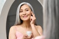 Happy middle aged mature asian woman looking at mirror applying antiage cream. Royalty Free Stock Photo