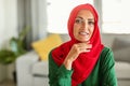 Happy middle aged muslim woman wearing red hijab, posing and smiling at camera, sitting at home in living room interior Royalty Free Stock Photo