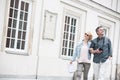Happy middle-aged tourist couple walking arm in arm by building