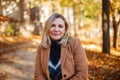 Happy middle-aged woman enjoying autumn outside, dressed in casual clothes and beige coat standing in yellow park