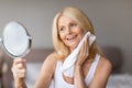 Happy middle aged woman looking at herself in mirror after shower, touching soft radiant skin on her face with towel Royalty Free Stock Photo