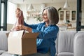 Happy middle aged woman opening parcel unpacking postal delivery box at home.