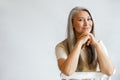 Happy middle aged woman with silver hair sits leaning on hands on light background