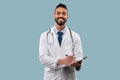 Happy Middle-Eastern Doctor Man Taking Notes Standing Over Blue Background Royalty Free Stock Photo