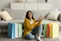 Happy Middle Eastern Lady Holding New Shoe, Sitting On Floor Among Colorful Shopper Bags And Smiling At Camera
