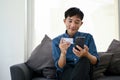 Happy Asian man using a mobile banking to pay his bills while relaxing in a living room Royalty Free Stock Photo