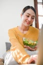 Happy millennial Asian woman eating healthy salad vegetables mix while using her laptop Royalty Free Stock Photo