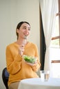 Happy millennial Asian woman having lunch, enjoys eating healthy salad vegetables mix at home Royalty Free Stock Photo