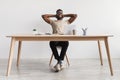 Happy millennial black man relaxing after work, putting feet on table at home office, full length Royalty Free Stock Photo