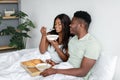 Happy millennial black wife and husband eat porridge on white bed in bedroom, enjoy breakfast and good morning Royalty Free Stock Photo