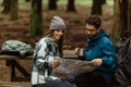 Happy millennial caucasian lady and man in jackets with backpack take break in cold forest, watch map